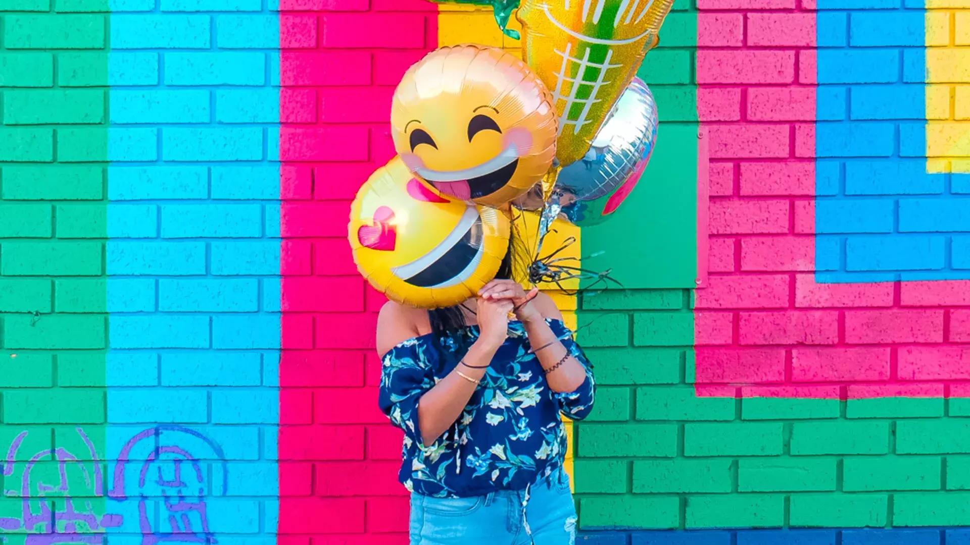 A girl celebrates her birthday with balloons in front of a colorful mural.
