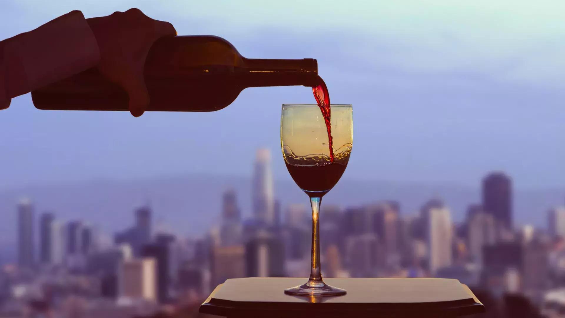 Un verre de vin rouge est servi, avec l'horizon de San Francisco visible par la fenêtre.