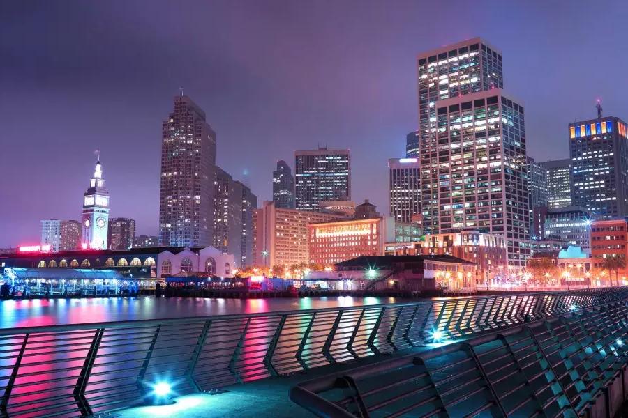 San Francisco's Embarcadero is lit up at night in an array of pastel colors.