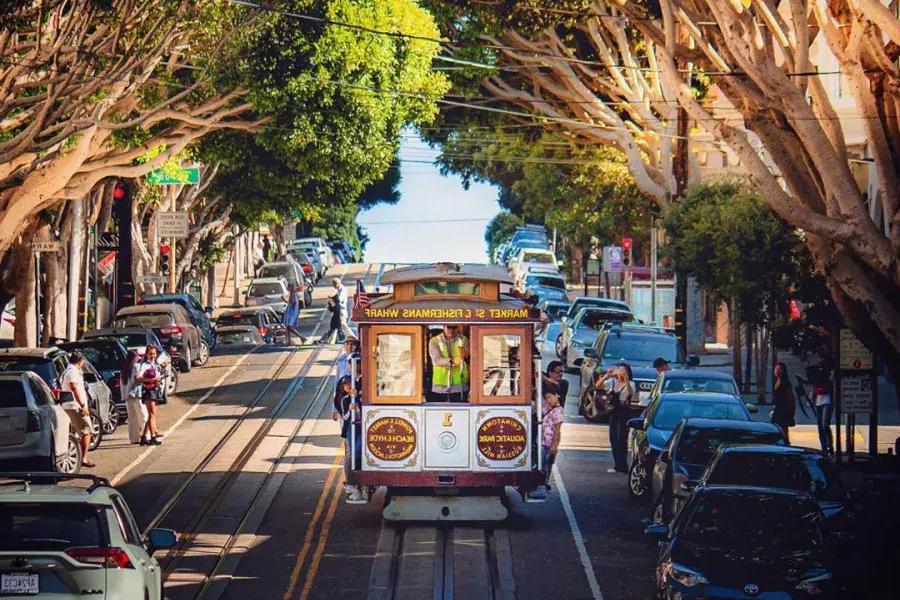 Un téléphérique de San Francisco s'approche dans une rue bordée d'arbres.