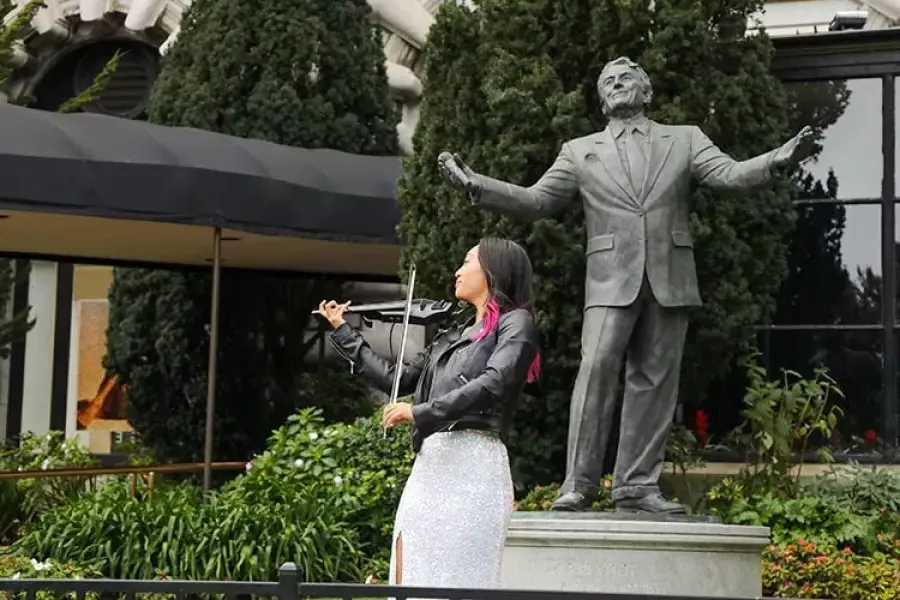 A woman plays the violin in front of the Tony Bennett statue at the Fairmont Hotel.