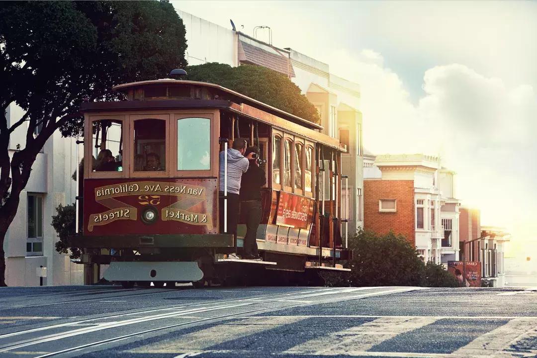 A cable car rounds a hill in San Francisco with passengers looking out the window.