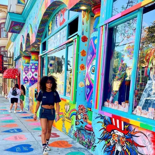 Mulher andando pela Haight Street com um mural colorido ao fundo.